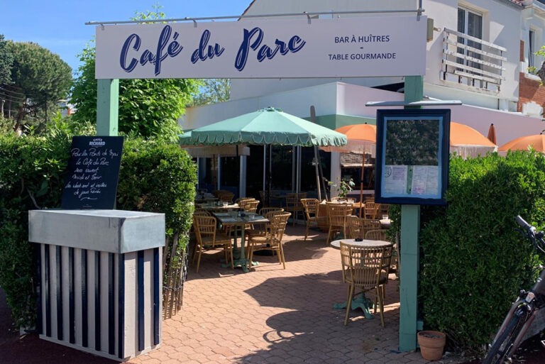 Mise en situation de l'identité visuelle créée par Gaëlle Geay : enseigne extérieure du Café du Parc surplombant une terrasse ensoleillée avec parasols et mobilier en rotin.